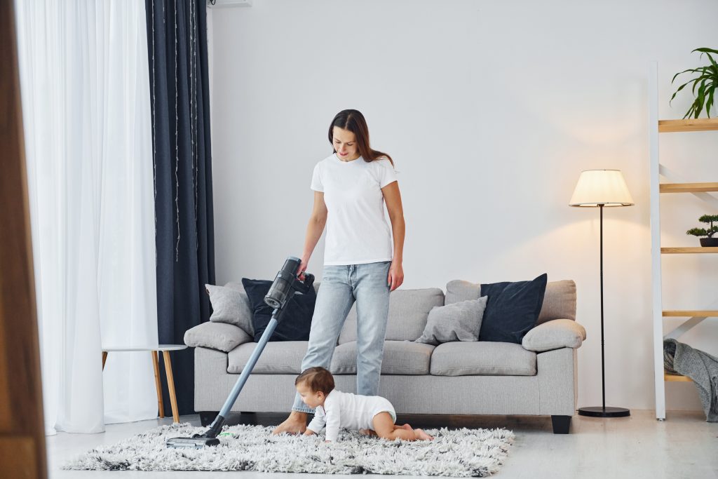 Cleaning floor by using vacuum cleaner Mother with her little daughter is indoors at home together