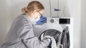 Scientist in laboratory coat loading textile samples into washing machine for antibacterial activity testing at Airmid Healthgroup laboratory.