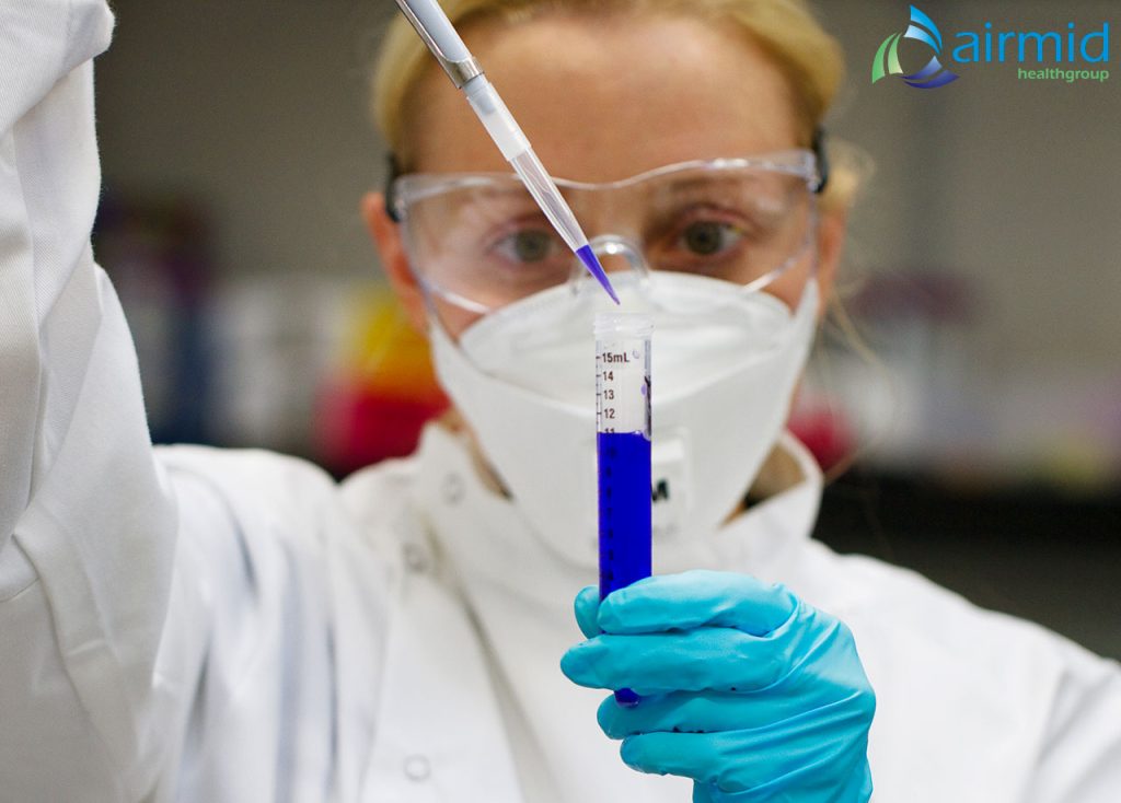 Scientist in PPE using a pipette to analyze test samples in a laboratory setting as part of antimicrobial technology validation at Airmid Healthgroup.
