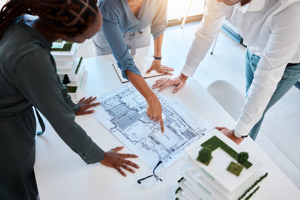 Architects Planning Sustainable Building Design with Blueprints | Airmid Healthgroup Architects reviewing blueprints and sustainable building models during a planning meeting