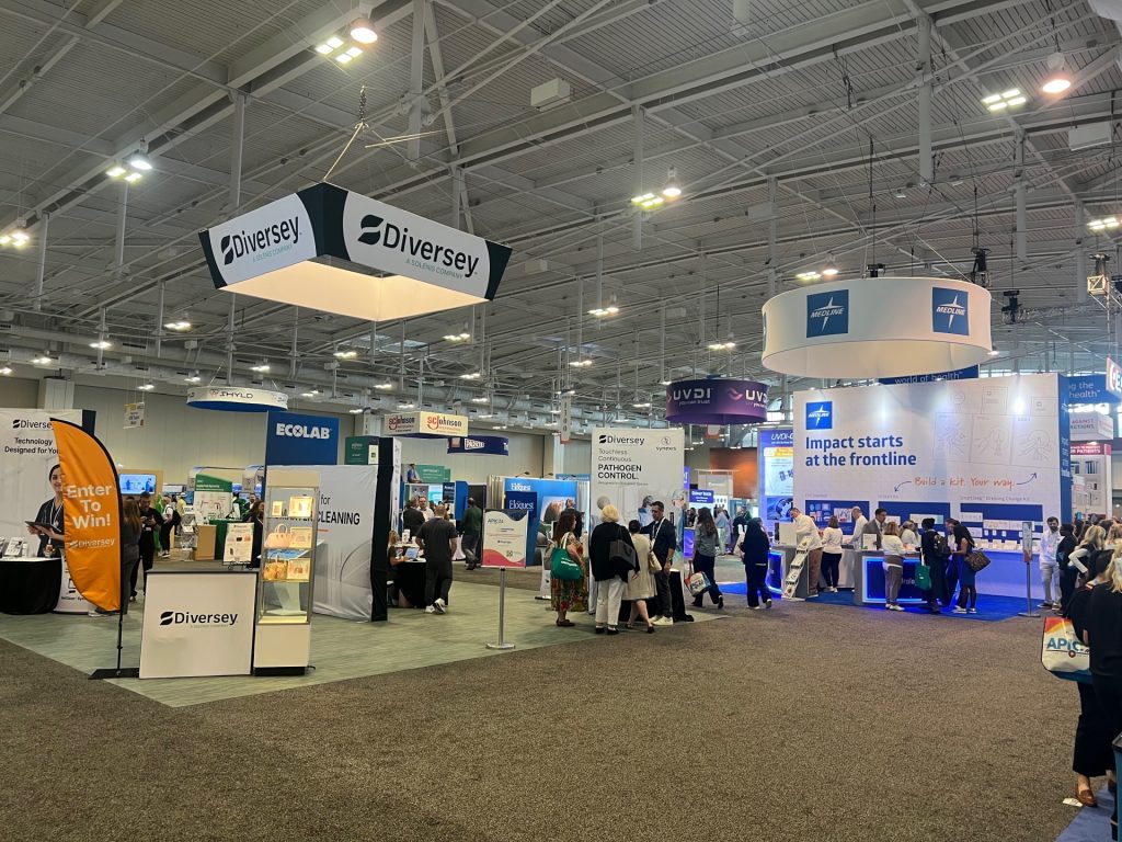 Busy expo hall at APIC 2026 in Nashville showing exhibitor booths including Diversey and Medline, with infection prevention professionals browsing the floor.
