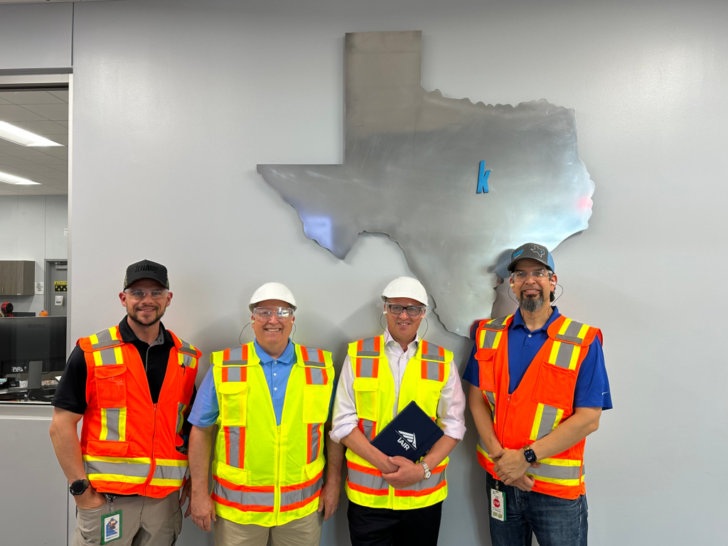 Dr John McKeon and Knauf Team Inside McGregor Facility Texas Map | Airmid Healthgroup Dr. John McKeon with three Knauf team members in hi-vis vests inside the McGregor facility, in front of a large Texas state wall installation