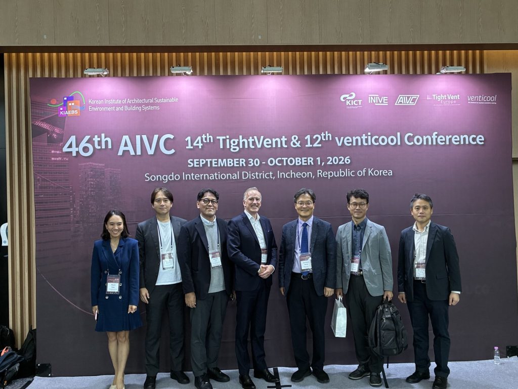 Dr. John Ryan of Airmid healthgroup standing with ASHRAE South Korea Chapter officers and AIVC 2026 conference organisers in front of the 46th AIVC Conference backdrop in Songdo, Republic of Korea