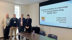 : Dr. Matthew Hardwick and fellow speakers beside a slide on germicidal UV testing using ASHRAE 185.1 at IUVA Americas 2026