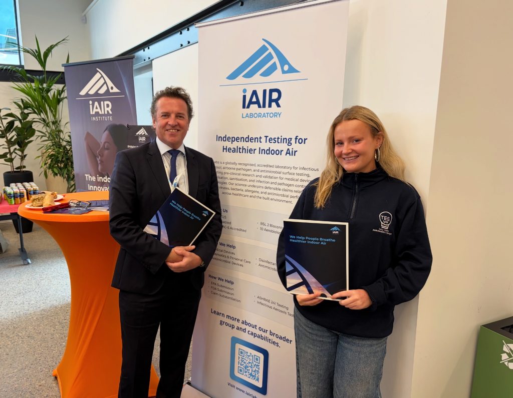 Dr John McKeon and Lucy Canny at Trinity Innovation Hub | Airmid Healthgroup Dr John McKeon and Trinity College Dublin student Lucy Canny holding iAIR brochures beside an iAIR Laboratory banner